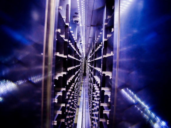 Abstract photo of supercomputer racks with blue, purple and shimmering white highlights. You feel drawn down a corridor of information