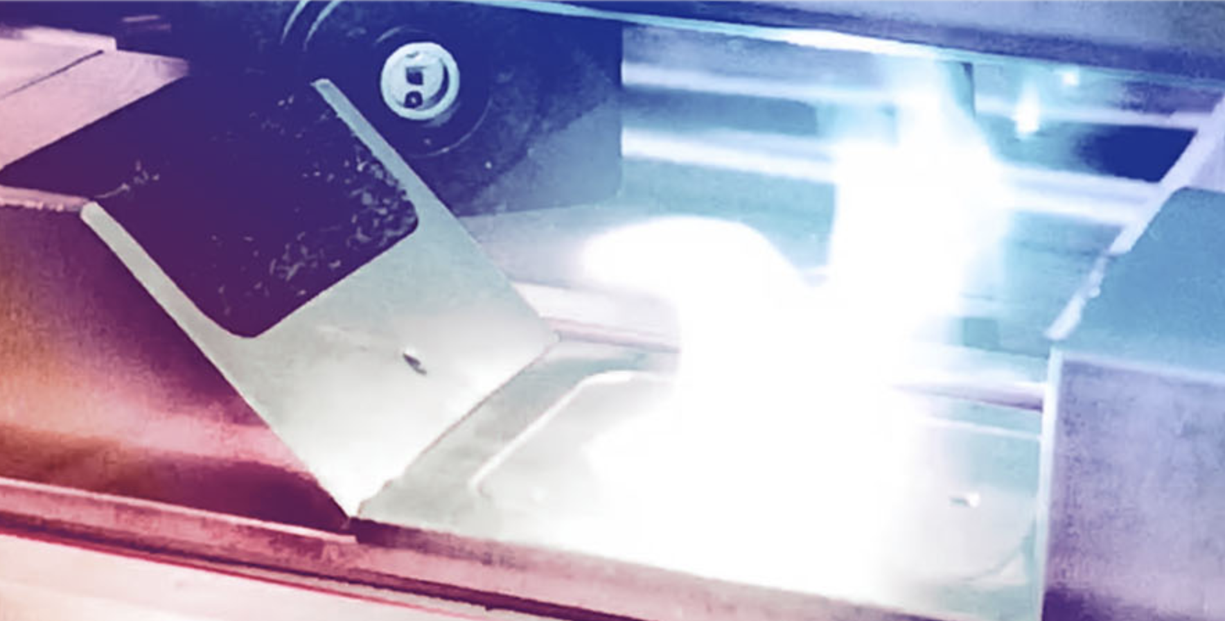 Photograph of metal machinery with glowing cyan material being processed