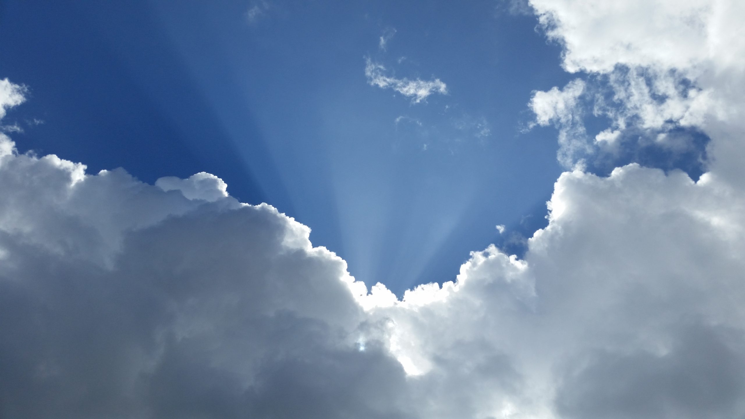 Photograph of a white and grey cloudy sky with sun rays peeking through the clouds