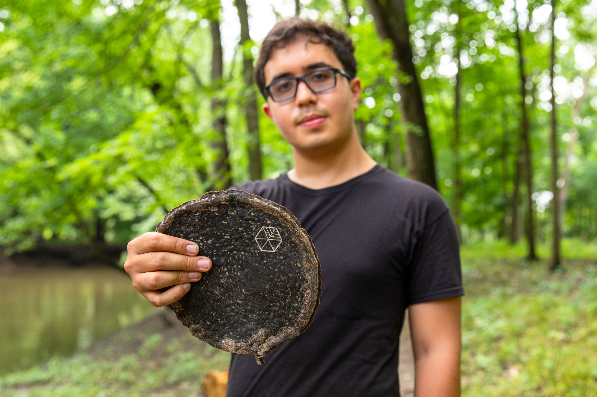 Gabe Tavas standing in a forest preserve surrounded by trees holding a rounded piece of Pyrus, the wood alternative.